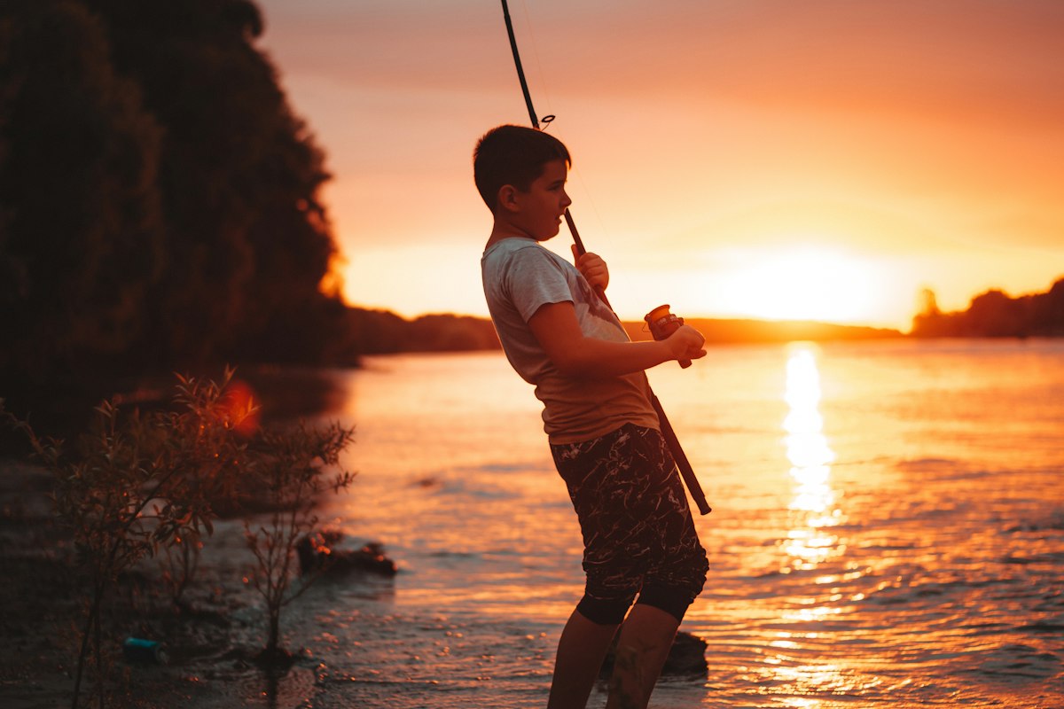 Niño sujetando una caña de pescar al atardecer